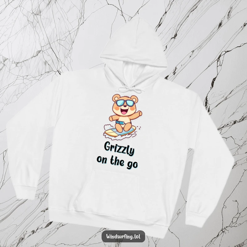 Funny hoodie with a cheerful bear windsurfing, grinning widely, conveying excitement and fun, perfect for cozy, humorous wear.
